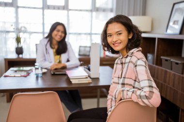 female patient smiling at the camera with a blurred background the doctor in the room looks