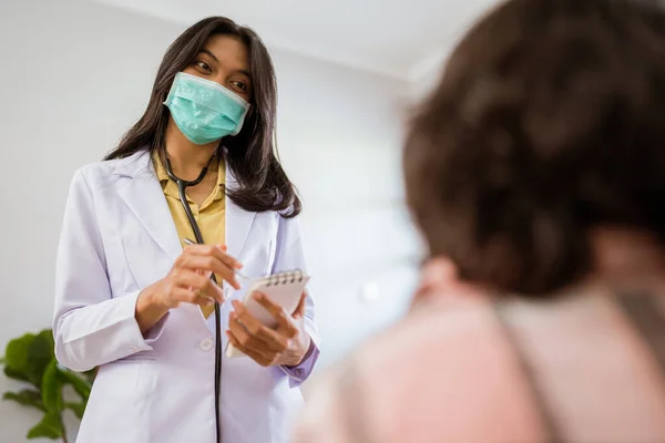 Female Doctor Wearing Mask Holding Note Pen While Examining Patient — Stock Fotó