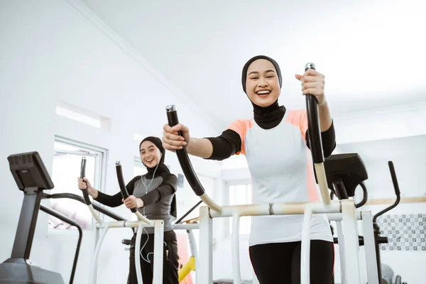 two beautiful woman with hijab at the gym exercising with friend on static elliptical cycle machine together