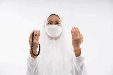 Woman in hijab wearing ihram praying al fatihah with prayer beads on isolated background