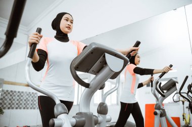 muslim women at the gym doing cardio exercises on static elliptical cycle machine