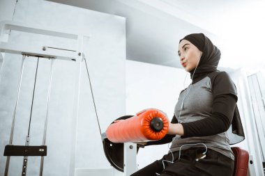 muslim asian woman working on her lower body using leg machine at the gym