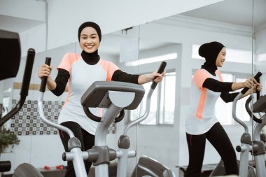smiling beautiful women at the gym doing exercises on static elliptical cycle machine