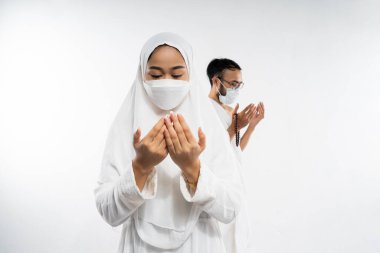 Asian woman wearing ihram clothes and mask with two palms up in prayer on isolated background