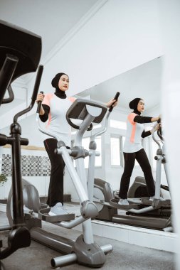 muslim women at the gym doing cardio exercises on static elliptical cycle machine