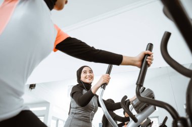 two beautiful woman with hijab at the gym exercising with friend on static elliptical cycle machine together