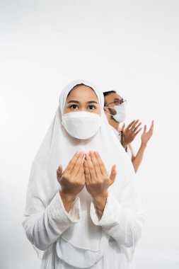 Woman wearing ihram clothes and mask with two palms up in prayer on isolated background