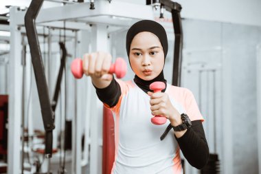 Asian muslim woman doing exercise, lifting dumbbell at the gym