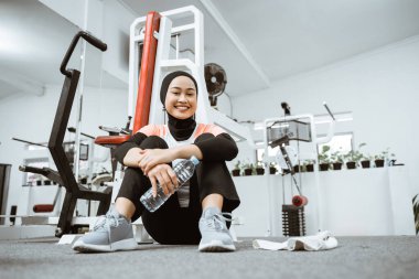 Young muslim woman sitting on a floor at gym after workout taking rest after fitness training at gym smiling to camera