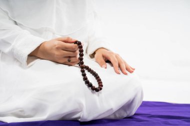 Womans hand wearing ihram praying with prayer rug and prayer beads on isolated background