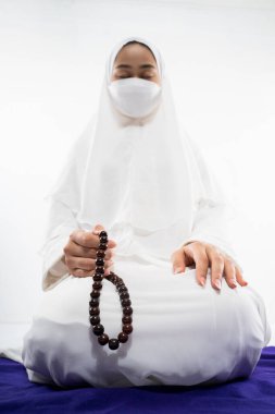 Woman wearing mukena praying with prayer beads on isolated background