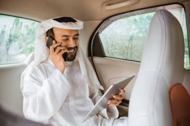 young man in a turban is calling using a mobile phone while sitting on his car