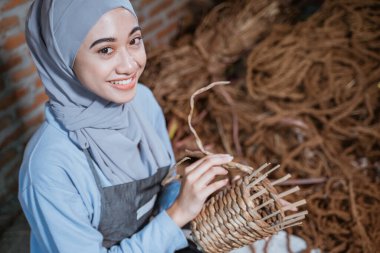 Smiling in veil craftswoman holding woven water hyacinth basket inside village house