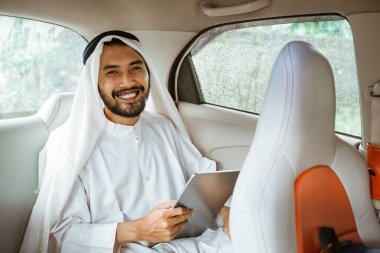 muslim asian man wearing turban using a pad while sitting on his car