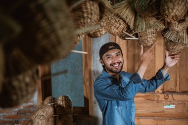 Bearded asian man smiling while holding water hyacinth handicrafts hanging in the village house