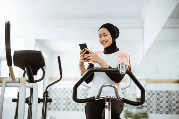 Attractive Muslim Woman Using Mobile Phone Exercising Static Bike Gym — 图库照片