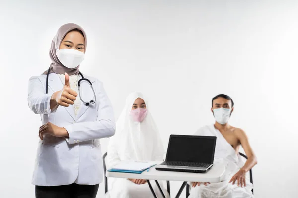 Veiled asian doctor in mask with thumbs up while standing against the background of prospective pilgrims