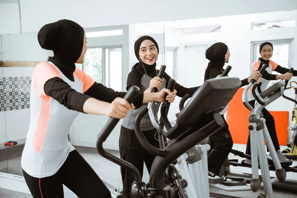 two beautiful woman with hijab at the gym exercising with friend on static elliptical cycle machine together