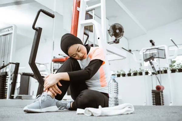 Young muslim woman sitting on a floor at gym after workout and looking down. Female athlete taking rest after fitness training at gym