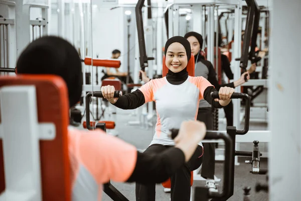 beautiful muslim asian woman using chest press machine during fitness at the gym with friend