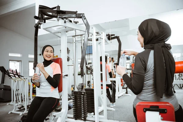 beautiful muslim asian woman using chest press machine during fitness at the gym with friend