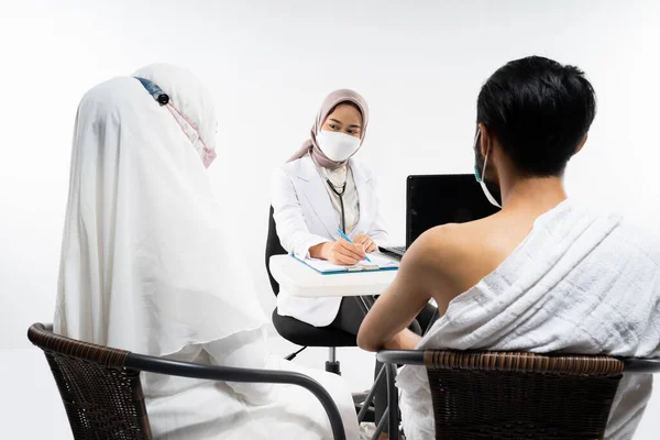 Doctors in masks chat with prospective pilgrims who are sitting in the room