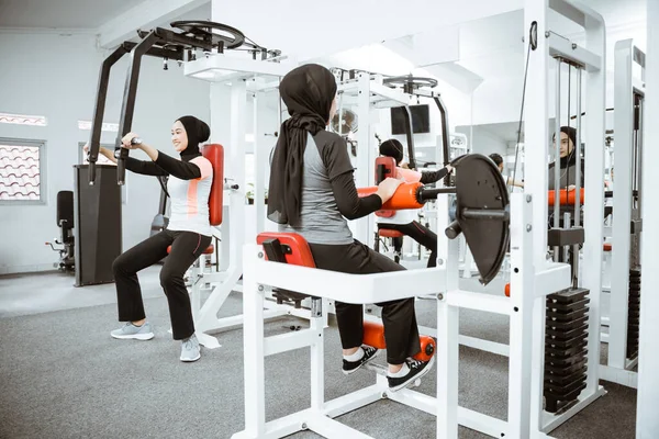 beautiful muslim asian woman using chest press machine during fitness at the gym with friend