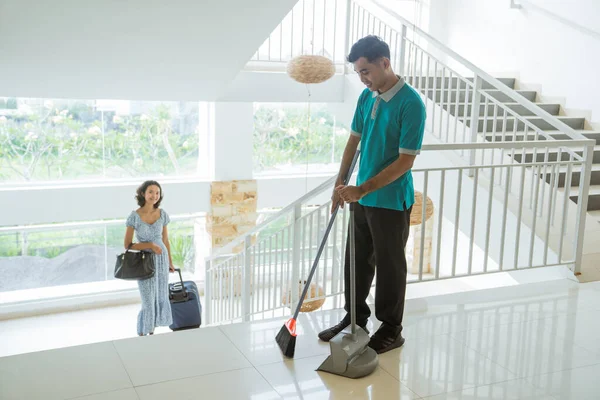 Janitor Wearing Turquoise Uniform Sweeps Female Guests Carry Bags Suitcases — Stockfoto