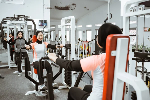 beautiful muslim asian woman using chest press machine during fitness at the gym with friend