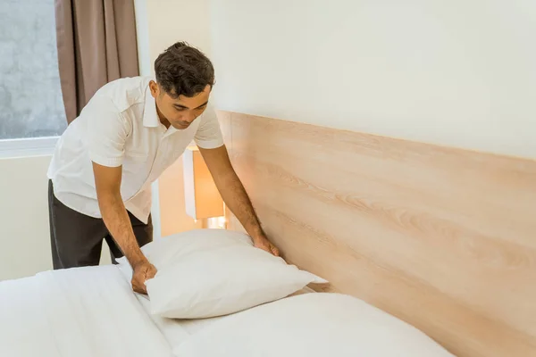 Asian male cleaning staff tidying pillows on bed in hotel room