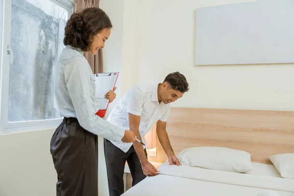 Female Housekeeper Carrying Clipboard Notes While Supervising Maid Cleaning Bed — 图库照片