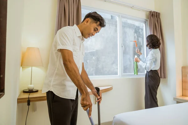 male cleaning staff sweeping with female staff wiping the hotel room window