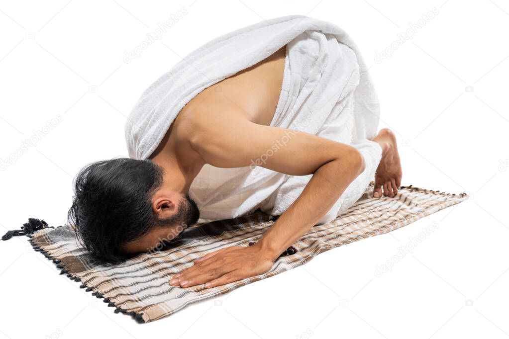 Man wearing ihram clothes praying with prayer rug while prostration on isolated background