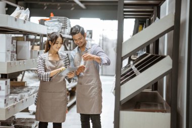 man and woman wearing aprons using a pad standing between shelves in glassware shop