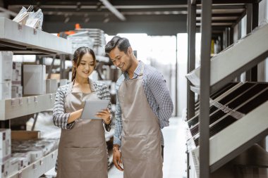 Boy and girl wearing apron using digital tablet while standing in aisle between storefront shelves
