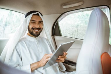 muslim asian man wearing turban using a pad while sitting on his car