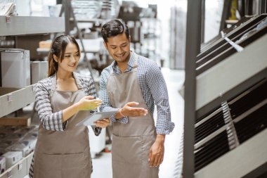 Boy and girl wearing aprons using a pad while checking items on shelves in houseware store