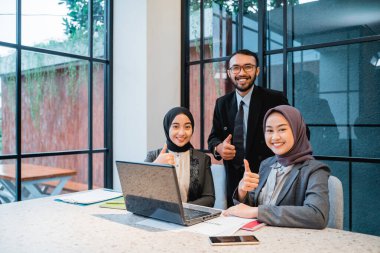 Ofiste otururken iş ekibinin baş parmağını göstermesi. Müslüman insanlar kameraya gülümsüyor.