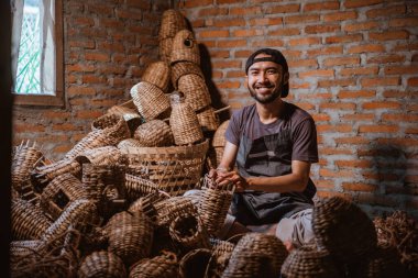 Water hyacinth craftsman smiling while making a basket against a brick wall background