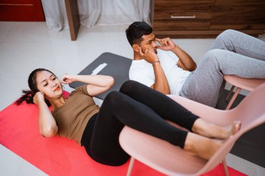 beautiful woman and husband doing sit up together using chair. couple doing partner exercising at home