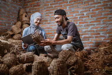 craftswoman in veil holding tablet and craftsman holding a woven water hyacinth craft in brick house