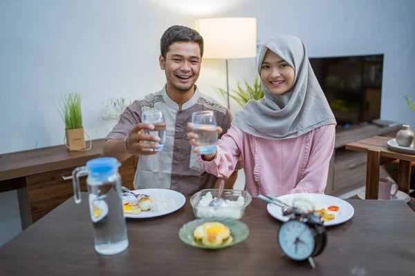 muslim couple wake up early to have sahur or suhur breakfast for fasting. clock at foreground showing the time