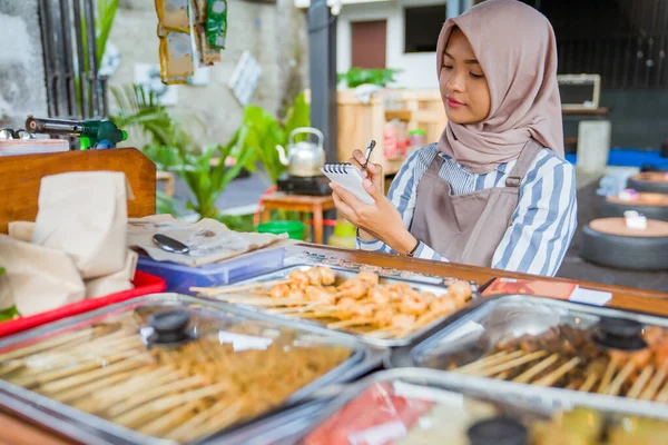 幸せなイスラム教徒の女性は仕事の終わりに彼女の食品事業の報告書を書きます — ストック写真