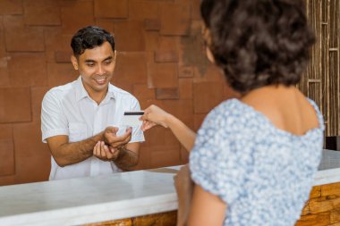 The receptionist accepts credit card payments from female guests in the hotel lobby