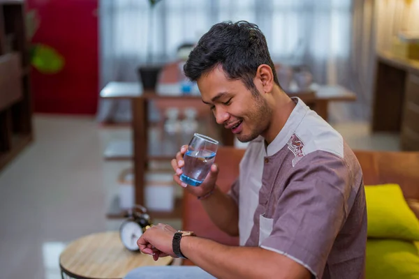 幸せなイスラム教徒の男性は彼の時計を見ながら水のグラスを保持断食を破るのを待っている — ストック写真
