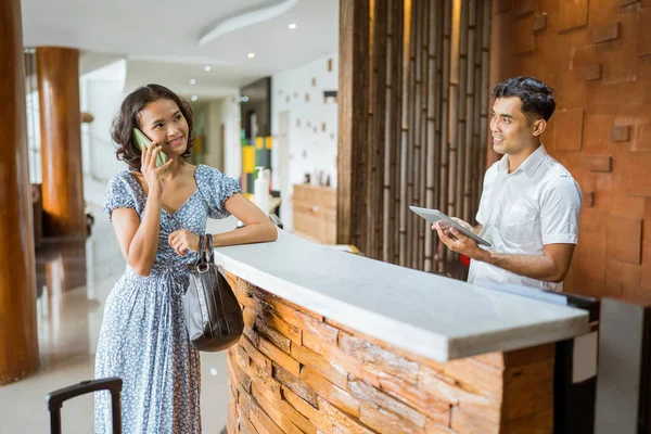 Asian Female Guest Calling Using Smartphone While Receptionist Using Tablet — Stockfoto