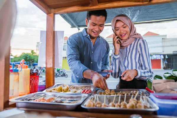 muslim couple ordering food to break fasting in traditional food market stall served by the seller