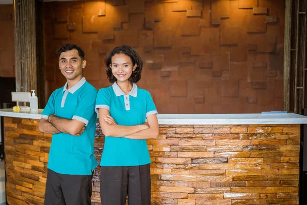 Two Receptionists Standing Smiling Hands Crossed Reception Desk Background — 图库照片