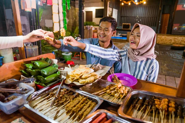 muslim couple ordering food to break fasting in traditional food market stall served by the seller