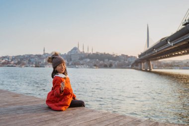 little girl with red coat sitting while looking at beautiful bosphorus istanbul turkiye